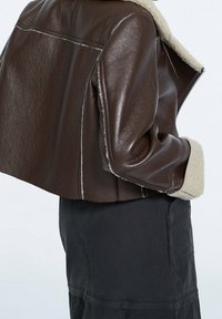 Brązowa skórzana kurtka z kołnierzem i mankietami z baranka, o przemyślanej konstrukcji, krótka długość i detale z kontrastującymi przeszyciami.