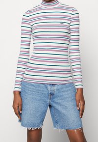 Haut à manches longues côtelé avec des rayures horizontales multicolores, doté d'un col montant et d'un petit logo brodé. Associé à un short en denim déchiré.