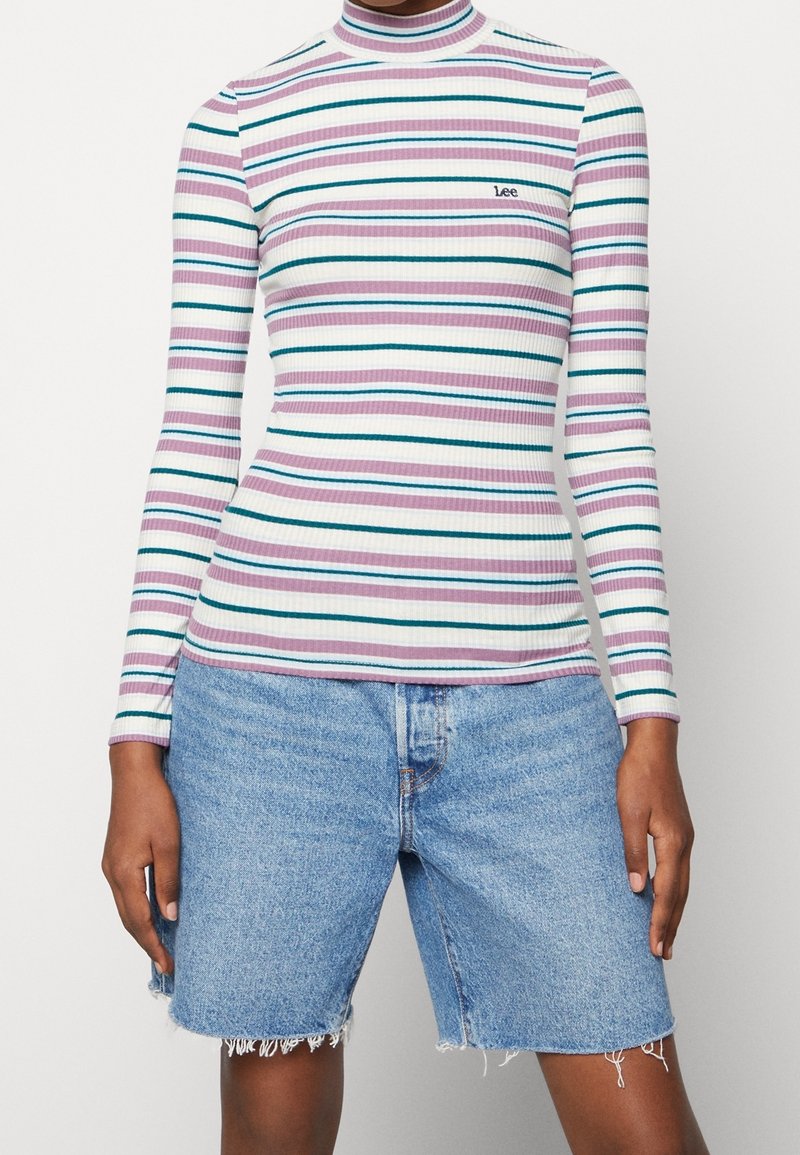 Haut à manches longues côtelé avec des rayures horizontales multicolores, doté d'un col montant et d'un petit logo brodé. Associé à un short en denim déchiré.