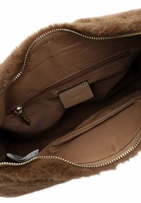 Intérieur d'un sac en fausse fourrure marron avec un doublage en tissu lisse, une poche zippée, une poche plate et une étiquette en cuir texturé. Détail en métal argenté sur la fermeture éclair.