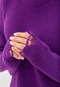 Maglione viola lavorato a maglia con maniche lunghe e aperture per il pollice. Il materiale è testurizzato con un motivo a coste, mostrando sfilacciature visibili sui polsini.
