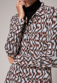 Chemise à manches longues à boutons présentant un motif ondulé en rouge, noir et blanc. Fabriquée en tissu tricoté avec une texture douce et un col classique.