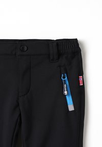 Sorte softshell-bukser med elastisk midje, glidelåslomme med blå detaljer, og norsk flagg-lapp. Glatt tekstur, funksjonell design.