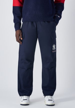 Navy cargo pants made from lightweight fabric, featuring two side pockets, elastic cuffs, and embroidered NY logo. Paired with white sneakers.