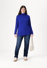 Blue long-sleeve turtleneck top paired with dark blue jeans. The top has a relaxed fit, and the outfit is complemented by a light bag.
