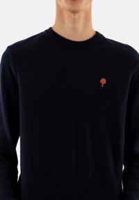 Maglione blu navy a collo rotondo, con un piccolo logo di un albero rosso sul petto. Texture morbida e tessuto di peso medio.
