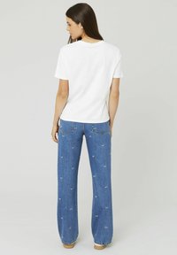 T-shirt en coton blanc associé à un jean en denim bleu, avec des détails brodés. Le jean a une coupe droite et un design de poche subtil.