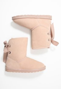 Botines de ante rosa que presentan una parte superior redondeada, lazos decorativos, ojales de metal y una suela de goma texturizada.