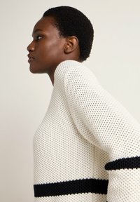 Strickpullover in Creme mit strukturiertem Muster, versehen mit schwarzen Streifen am Saum und an den Ärmeln. Lockere Passform mit einem Boot-Ausschnitt.