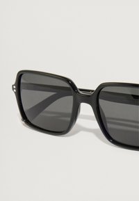 Μαύρα ορθογώνια γυαλιά ηλίου με πολωμένους σκούρους φακούς. Διαθέτουν ομαλό πλαστικό σκελετό και κομψό σχέδιο γέφυρας. Δεν υπάρχουν ορατές λεπτομέρειες υλικών.