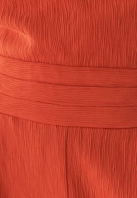 Pruhovaná oranžová látka s hladkým elastickým pásom. Textúra obsahuje opakujúce sa vertikálne línie, ktoré pridávajú rozmer a zaujímavý vzhľad.