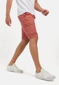 Männer Cargoshorts in Korallenfarbe mit Seitentaschen und gesteppten Details, kombiniert mit weißen Sneakern mit grauen Akzenten und Schnürdesign.