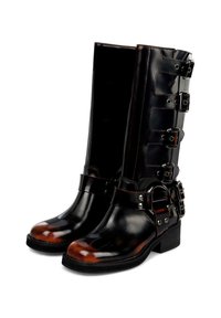 Stivali neri alti fino al ginocchio in pelle con finitura lucida, caratterizzati da quattro fibbie argentate regolabili e puntale marrone testurizzato. Tacco nero solido.
