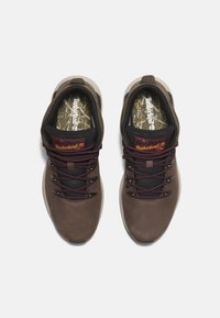 Bruna vattentäta skor med svarta accenter, strukturerade sidor och vinröda snören. Har en mönstrad innersula med Timberland-logotyp.