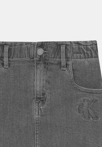 Šedé džíny z denimu s elastickým pasem, standardními kapsami a vyraženým logem 'cK' na přední straně. Hladká textura a klasický střih.