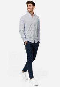 Himmelblaues Hemd mit kleinem Muster, kombiniert mit navyblauen Hosen und weißen Sneakern, präsentiert in einer lässigen Gehpose.