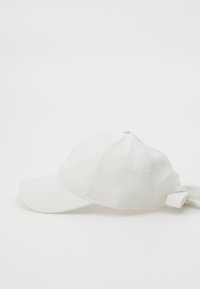 Gorra blanca con tejido texturizado, visera curvada y un lazo ajustable en la parte trasera para un ajuste seguro. Diseño simple con una estética limpia.