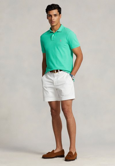 Πράσινο πόλο μπλουζάκι με κοντά μανίκια, λευκά σορτς και καφέ μοκασίνια. Σημαντικές λεπτομέρειες περιλαμβάνουν ένα μικρό λογότυπο και μια ταμπά ζώνη.