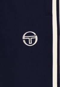 Marineblått stoff med en teksturert overflate, med et hvitt emblem og to hvite striper langs siden. Rent og minimalt design.