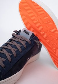 Sneaker in suede blu navy con lacci grigi, suola bianca e suola in gomma arancione vivace con un motivo a zigzag. Logo sulla linguetta.