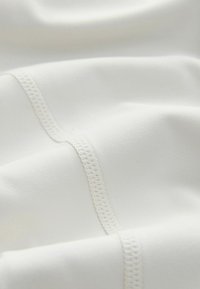 Tissu blanc doux avec deux coutures parallèles visibles présentant une couture détaillée, montré en gros plan avec des plis doux.