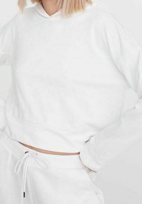 Vit kort croppad hoodie med långa ärmar, tillverkad av mjukt tyg, med dragsko vid halsen och en avslappnad passform.