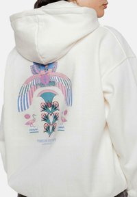 Sudadera color crema con un diseño gráfico en la parte posterior que presenta patrones coloridos de plantas, aves y formas geométricas. Tejido suave y corte relajado.