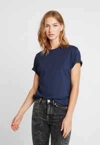 Navy blue cotton t-shirt with rolled sleeves, round neckline, and relaxed fit, paired with faded black jeans. Smooth texture, minimal detailing.