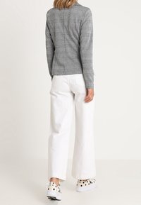 Šedé kárované přiléhavé tričko s dlouhým rukávem spojené s bílými kalhotami s širokými nohavicemi a černobílými slip-on botami s puntíky.