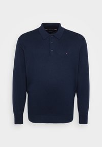 Granatowy sweter polo z długim rękawem z trzema guzikami oraz małym logo w kolorach czerwonym, białym i niebieskim po lewej stronie klatki piersiowej.