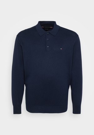 Tumesinise pika varrukaga polo-sviiter, millel on kolm nuppu ja väike punane, valge ja sinine logo vasakul rinnaosal.