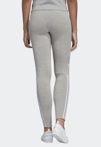 Leggings grigi realizzati in tessuto morbido, con strisce laterali bianche, una silhouette aderente e una texture liscia.