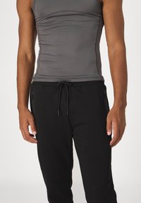 Grå tætsiddende tanktop med sammensunkne sider, parret med sorte joggingbukser med justerbar snøre og sidelommer med lynlås.