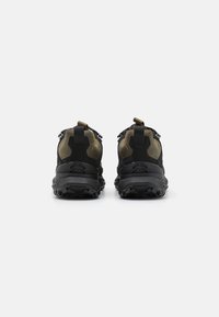Zwarte en olijfkleurige wandelschoenen hebben een gestructureerde bovenkant, een robuuste zool en rubberen accenten, met een trekband aan de achterkant voor eenvoudig aan- en uittrekken.