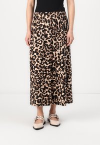 Pantalons ample à imprimé léopard en beige et noir, avec une taille élastique. Portés avec des chaussures légèrement colorées, ornées de sangles.