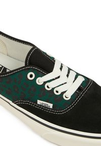 Mustekala- ja vihreällä leopardikuosilla varustetut kangaskengät, joissa on valkoiset nauhat, mustat mokkanahkaosat ja valkoinen kumipohja.