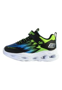 Scarpa sportiva nera e verde neon con tomaia in materiale sintetico, design in rete traspirante, motivo a zigzag e suola bianca ammortizzata. Inclusa una fascia in velcro.