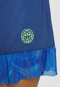 Námořnický modrý šaty s texturovaným, síťovým volánkem na spodním lemu v odstínech modré. Obsahuje zelenou logo emblému na horním levém rohu šatů.