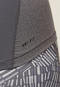 Haut de sport Dri-FIT avec une partie supérieure grise texturée à lignes verticales et une section inférieure à motifs de rayures horizontales blanches et grises.