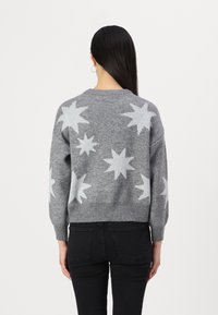 Pulover tricotat gri cu modele de stele albe, mâneci și tiv cu dantelă. Croială lejeră și design scurt, potrivit pentru îmbrăcăminte casual.