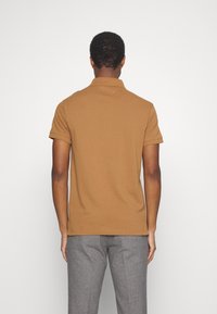 Polo shirt marron avec un design à col, des manches courtes et des détails côtelés, associé à un pantalon gris texturé.