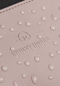 Világos rózsaszín vízálló anyag vízcseppekkel, az "JOHNNY URBAN" logó bélyegzett, fekete varrás, és sima textúra.