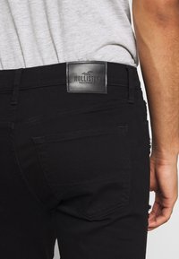 Svarta denimjeans med en läderlabel från Hollister på baksidan av midjebandet, med en åtsittande design, minimal sömnad och standardfickor.