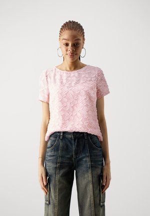 Top rosa de manga corta con diseño texturizado floral; combinado con pantalones de mezclilla anchos de pierna oscura que cuentan con bolsillos frontales y cierre de cremallera.