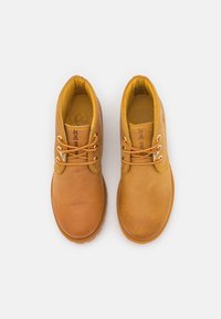 Botas de cuero marrón hasta el tobillo con acentos amarillos, punta redonda, ojetes metálicos y cordones naranjas. Superficie texturada con un acabado suave.