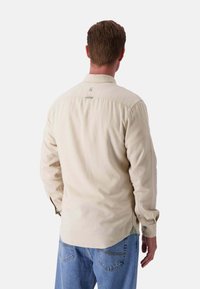 Camicia a maniche lunghe beige chiaro con colletto abbottonato, tessuto testurizzato e un accento verde all'orlo. Presenta un piccolo logo vicino al collo.