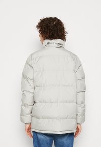 Šedá péřová bunda s prošívanými částmi a elastickými manžetami. Má vysoký límec s logem 'HELly HANSEN'. Hladký, lesklý materiál.