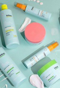 Zes haarverzorgingsproducten gerangschikt op een mintgroene achtergrond: lichtblauwe flessen, een roze ronde pot, een oranje spuitdop en witte crèmes.