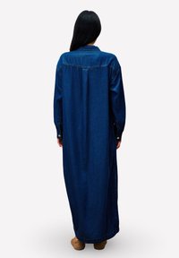 Langdenim jurk in donkerblauw, met een knoopmanchet, een zijslit en een klassieke kraag. Soepele textuur met zichtbare stikseldetails.