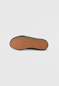 Semelle en caoutchouc noir avec un dessous texturé orange présentant un motif en losange pour une meilleure adhérence et stabilité. Le bord est arrondi.